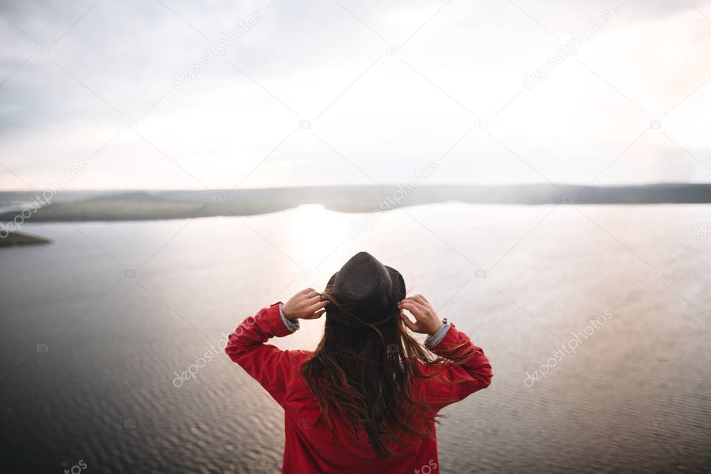 Traveler girl in hat and with windy hair standing in evening sun