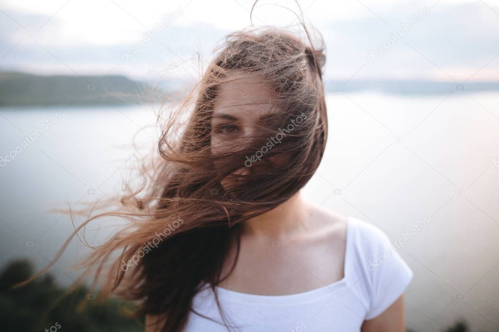 Portrait of hipster girl with windy hair standing on top of rock