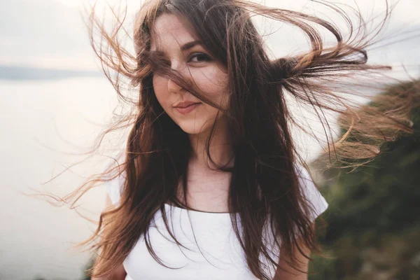 Portrait of hipster girl with windy hair standing on top of rock — Stock Photo, Image