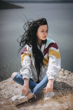 Rock moun üstünde oturan rüzgarlı saçlı şık hipster kız