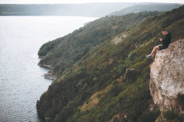 Hipster gezgin kaya dağın tepesinde oturan ve zevk
