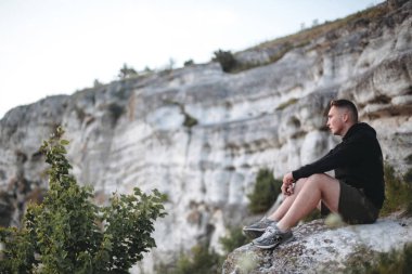 Hipster gezgin kaya dağın tepesinde oturan ve zevk