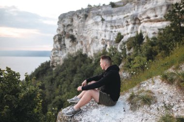 Hipster gezgin kaya dağın tepesinde oturan ve zevk