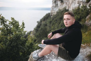 Hipster gezgin kaya dağın tepesinde oturan ve zevk