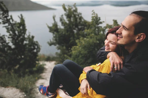Feliz pareja hipster en impermeables sentados en la cima de la roca mountai — Foto de Stock