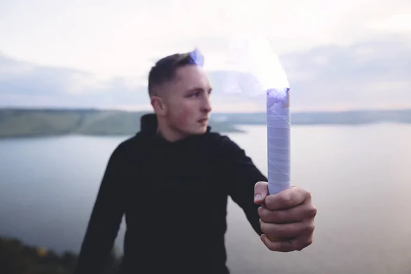 Brutal man in black windbreaker holding blue flare torch in hand — Stock Photo, Image