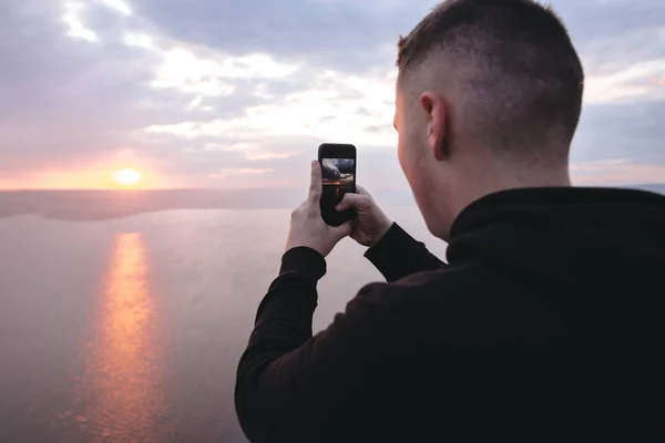 Hipster viajero tomando fotos en el teléfono de increíble puesta de sol vista en — Foto de Stock