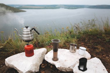 Çelik su ısıtıcısı gaz primus, metal kupalar ve aeropress üzerinde kaynayan 