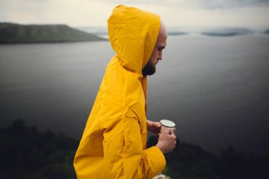 Sarı yağmurluk lu gezgin metal kupa tutan ve cl üzerinde duran