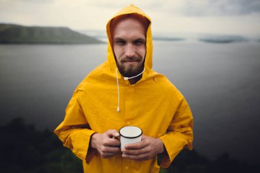 Metal kupa ve standi tutan sarı yağmurluk Hipster gezgin