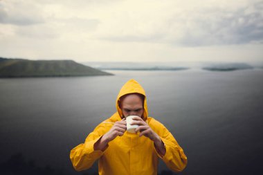 Metal kupa ve standi tutan sarı yağmurluk Hipster gezgin