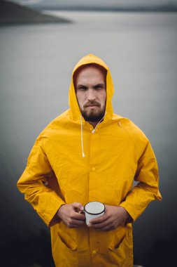 Sarı yağmurluk lu gezgin metal kupa tutan ve cl üzerinde duran