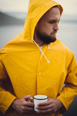 Sarı yağmurluk lu gezgin metal kupa tutan ve cl üzerinde duran