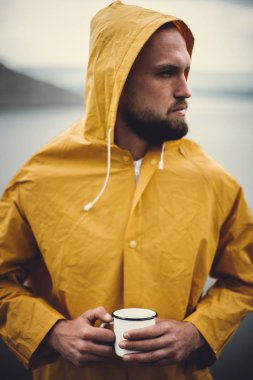 Sarı yağmurluk metal kupa ve trav tutan acımasız sakallı adam
