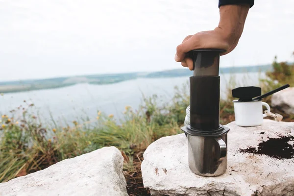 Voyageur pressant aération sur tasse métallique sur falaise au lac, brewi — Photo