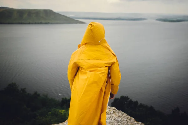 Man in yellow raincoat traveling on cliff and looking at lake in — Stock Photo, Image