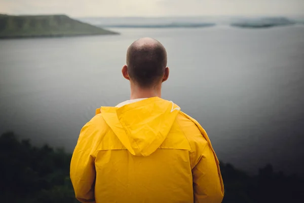 Hipster-Reisender in gelbem Regenmantel steht auf Klippe und blickt — Stockfoto