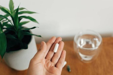 Ahşap ta su bardağı üzerinde magnezyum kapsül tutan El