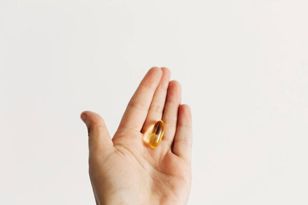 Hand holding omega 3 capsule on white wall background. Morning d
