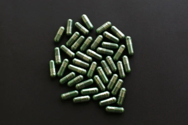 Spirulina capsules on black dark background. Flat lay. Dietary s