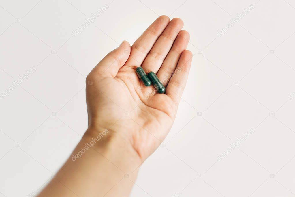 Dietary supplements. Hand holding spirulina capsules on white wa