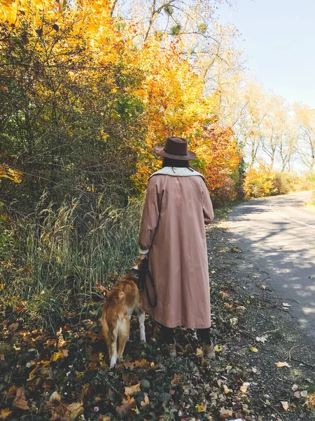 Hipster chica en sombrero y abrigo caminando con su perro de oro en autu —  Fotos de Stock