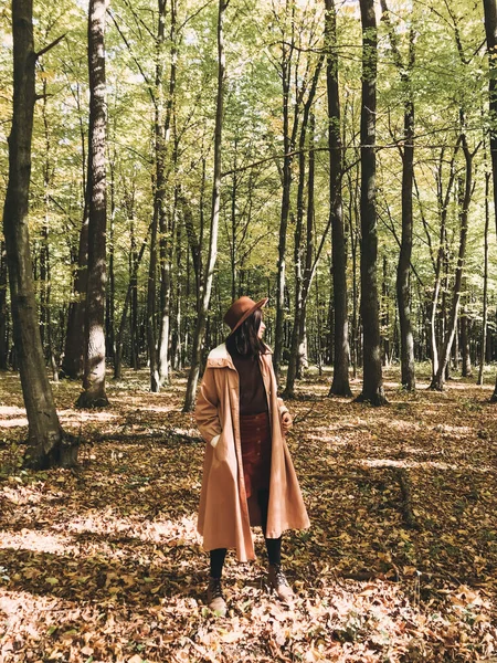 Хипстерша в шляпе и пальто, путешествующая осенью в солнечном лесу — стоковое фото