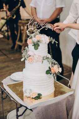 Gelin ve damat düğün resepsiyonunda şık bir düğün pastası kesiyorlar.