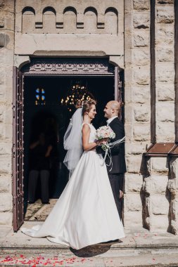 Güzel gelin, şık damatla öpüşüyor, kilisede duruyor.