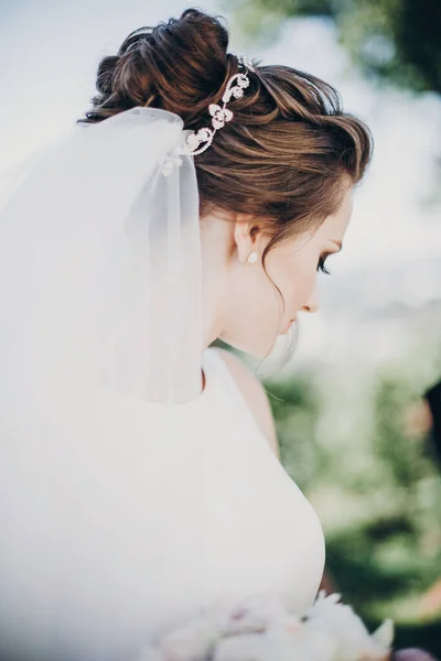 Hinreißende Braut im weißen Kleid mit stylischer Frisur und Schleier — Stockfoto