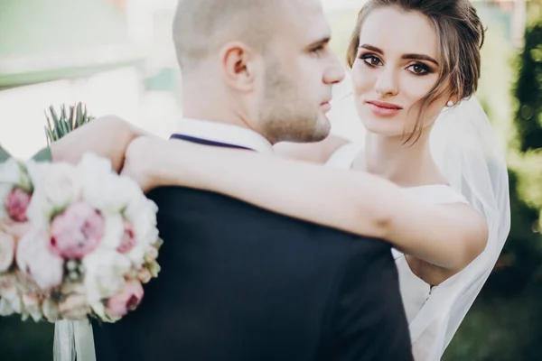 Linda noiva gentilmente abraçando noivo e segurando buquê de casamento — Fotografia de Stock