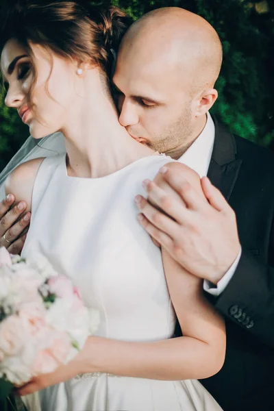 Groom gently kissing gorgeous bride on neck in sunset light. Por — Stock Photo, Image