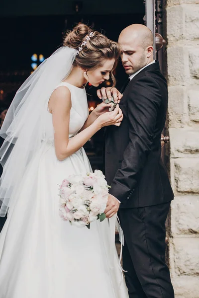 Krásná nevěsta dává stylové boutonniere na ženich oblek, stojí — Stock fotografie