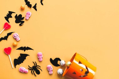 Mutlu Cadılar Bayramı düz yatıyordu, kopya alanı. Cadılar Bayramı şeker, kafatasları, siyah yarasalar ve hayalet kağıt süslemeleri sarı arka plan üzerinde kötü kova dağınık. Trick veya tedavi kavramı.