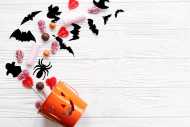 Kafatasları ile Halloween şeker, siyah yarasalar, hayalet, beyaz ahşap arka plan üzerinde jack o fener kova dökülen örümcek süslemeleri, düz yatıyordu. Cadılar Bayramı tatlıları. Kopya alanı. Hediye ver yoksa karışmam