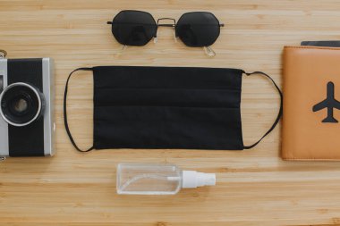 2020 yazında iyi yolculuklar. Siyah maske, antiseptik ve dezenfektan, pasaport, güneş gözlüğü ve tahta zemin üzerinde fotoğraf makinesi. Coronavirus tatil koruma tedbirleri