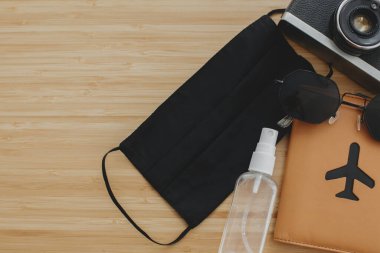 2020 yazında iyi yolculuklar. Siyah maske, antiseptik ve dezenfektan, pasaport, güneş gözlüğü ve tahta arka planda fotoğraf makinesi. Coronavirus tatil koruma tedbirleri