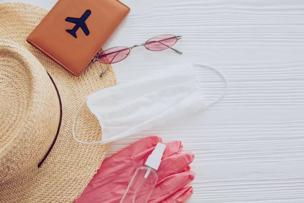 Summer vacation 2020. Face mask, pink gloves, antiseptic and disinfectant, passport, sunglasses, straw hat on white background. Safe travel and Coronavirus protection measures