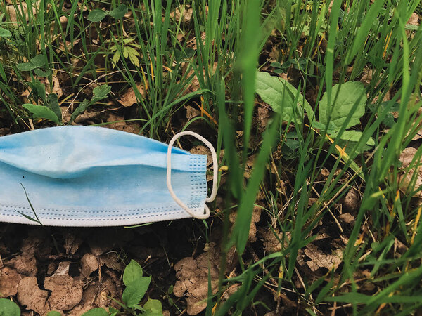 Disposable dirty face mask on ground, single use plastic trash on grass. Coronavirus plastic waste environmental pollution. How to dispose used medical masks right after coronavirus pandemic.