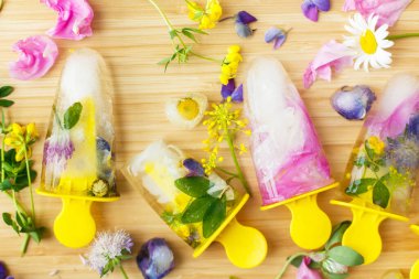 Çiçekli buzlu şeker dümdüz yatıyordu. Donmuş buzlu buzlu ve buzlu renkli kır çiçekleri ve tahta arka planda taze yaz çiçekleri. Yaratıcı bir imaj. Merhaba yaz konsepti.