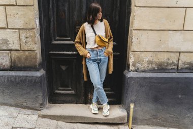 Avrupa şehir caddesindeki binada duran şık hippi kız. Eski ahşap kapıya poz veren modaya uygun giyinmiş genç bir kadın. Şehirde tek başına boş zaman aktivitesi