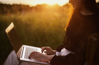 Serbest ve açık havada uzaktan çalışma. Günbatımında güneşli yaz sahasında oturan zarif bir kız. Bilgisayarda çalışan genç bir iş kadını. Yaratıcı resim