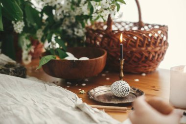 Modern balmumu süslemeleri ve sade ahşap masa üzerinde bahar çiçekleri, sepet, mum, keten kumaşlı doğal boyalı yumurtalarla süslü Paskalya yumurtası. Sıfır kayıp. Paskalya tarzı kırsal yaşam.