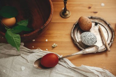 Modern balmumu süslemeleri olan şık Paskalya yumurtaları ve sade ahşap masa üzerinde bahar çiçekleri, mum ve keten kumaşlı doğal boyalı yumurta. Eko Sıfır israfı. Paskalya tarzı kırsal yaşam