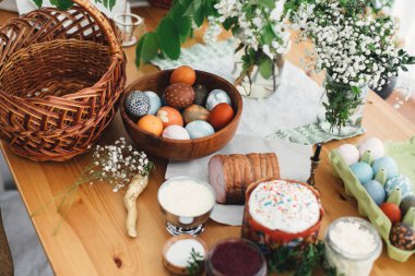 Paskalya hazırlıkları. Paskalya yumurtaları, paskalya ekmeği, jambon, pancar, tereyağı, yeşil dallar ve saman sepetli ahşap masa ve mum. Geleneksel Paskalya Yemeği