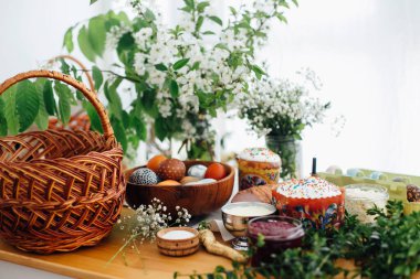 Paskalya yumurtaları, paskalya pastası, jambon, pancar, tereyağı, yeşil dallar ve saman sepetli ahşap masa üzerinde çiçekler. Tatil hazırlığı. Geleneksel Paskalya Yemeği