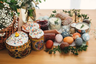 Paskalya brunch 'ı. Paskalya yumurtası, paskalya ekmeği, jambon, pancar, tereyağı, peynir, sosis, yeşil dallar ve kır ağacından bir masa üzerinde çiçekler. Tatil hazırlığı. Geleneksel Paskalya Yemeği.