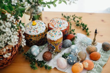 Paskalya pastası, doğal boyanmış Paskalya yumurtaları, mum, yeşil dallar ve hasır sepetli ahşap masa üzerinde çiçekler. Geleneksel Paskalya Yemeği Kilisede kutsanmak için