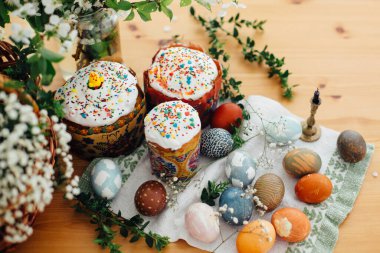 Kırsal masada geleneksel Paskalya yemeği. Ev yapımı paskalya pastası, doğal boyanmış paskalya yumurtaları, mum, yeşil dallar ve ahşap arka planda çiçekler. Kutsamak için Paskalya Yemeği