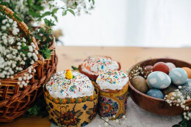 Kırsal masada geleneksel Paskalya yemeği. Ev yapımı paskalya pastası, doğal boyanmış Paskalya yumurtaları, mum, yeşil dallar ve ahşap arka planda hasır sepetli çiçekler. Kutsamak için Paskalya Yemeği